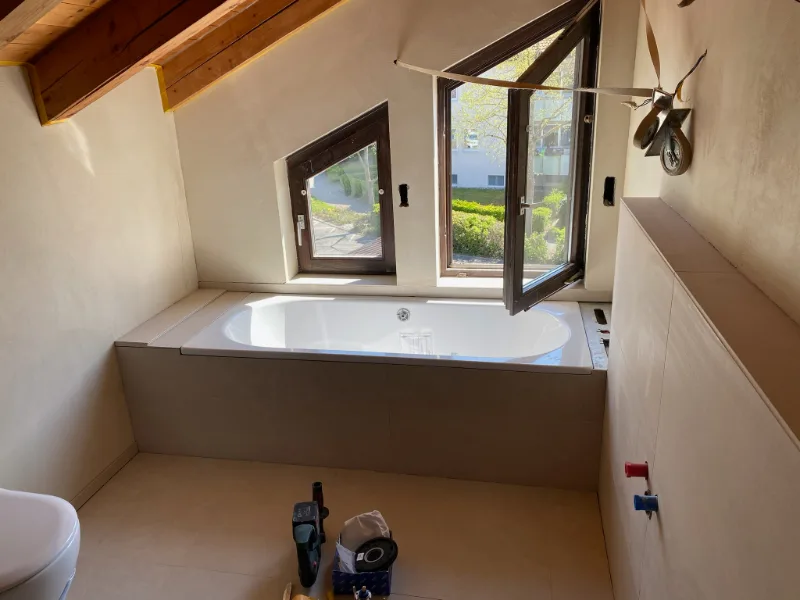 Dachbad im Ausbau: Badewanne unter der Dachschräge eingefliest, Wandanschlüsse für Waschtisch noch offen