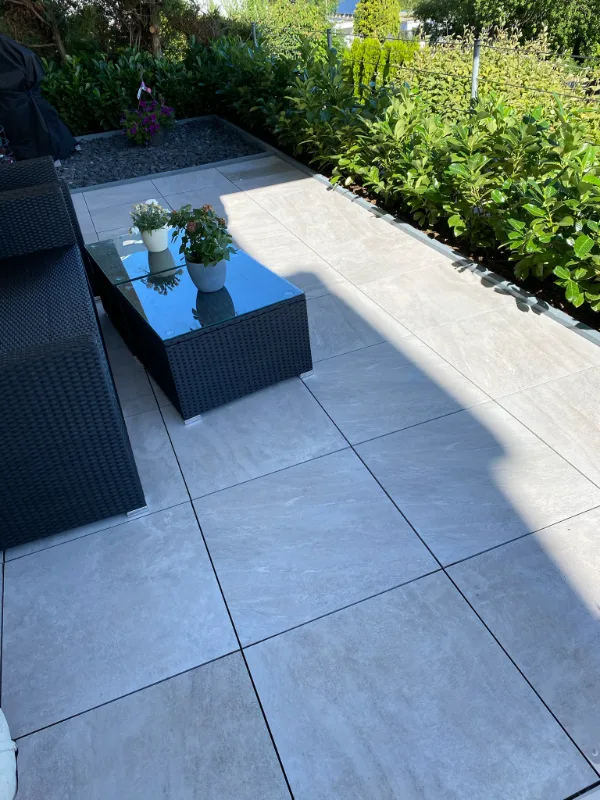 Fertige Dachterrasse mit großformatigem Plattenbelag, Sitzgruppe und Heckenpflanzung über den Dächern