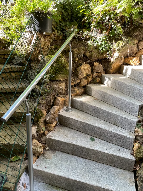 Neue Treppe aus Granit-Blockstufen mit Edelstahl-Handlauf, seitlich in die vorhandene Natursteinböschung eingebunden