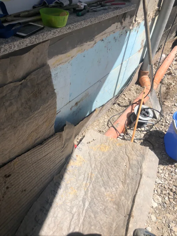 Erdberührte Kelleraußenwand: Bitumendickbeschichtung, davor Perimeterdämmung und Schutzvlies, im Graben Drainleitung und Kiesfilter