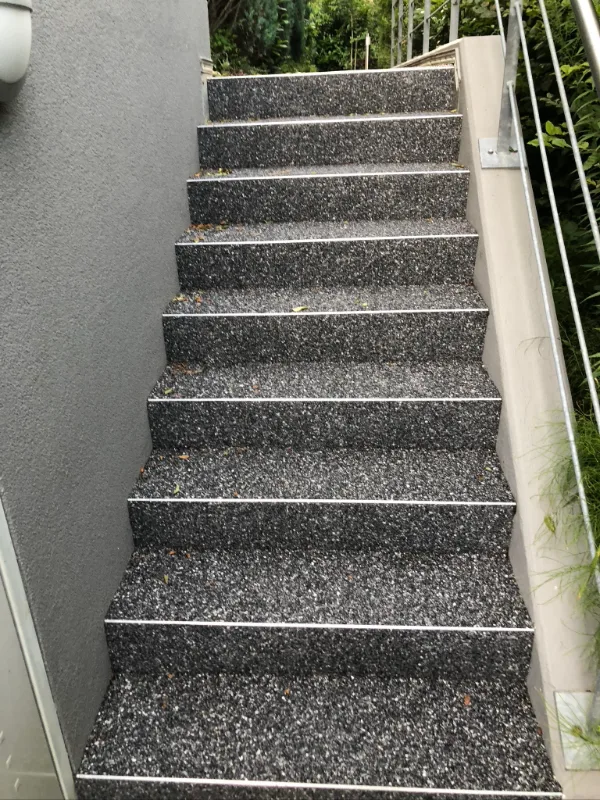 Außentreppe mit Steinteppich beschichtet, an jeder Stufenkante ein Abschlussprofil, seitlich Edelstahlgeländer